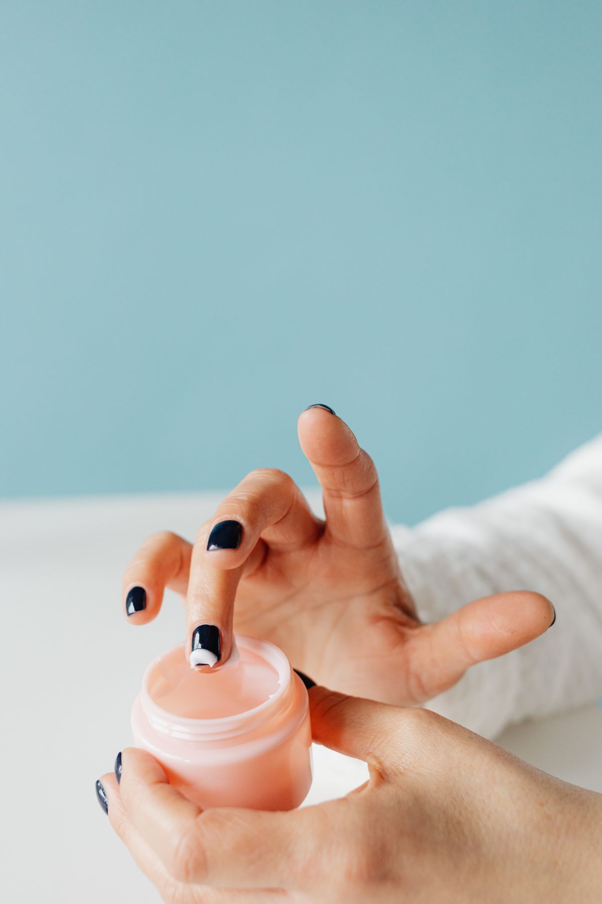 Hands lifting a rich cream from a small pink jar
