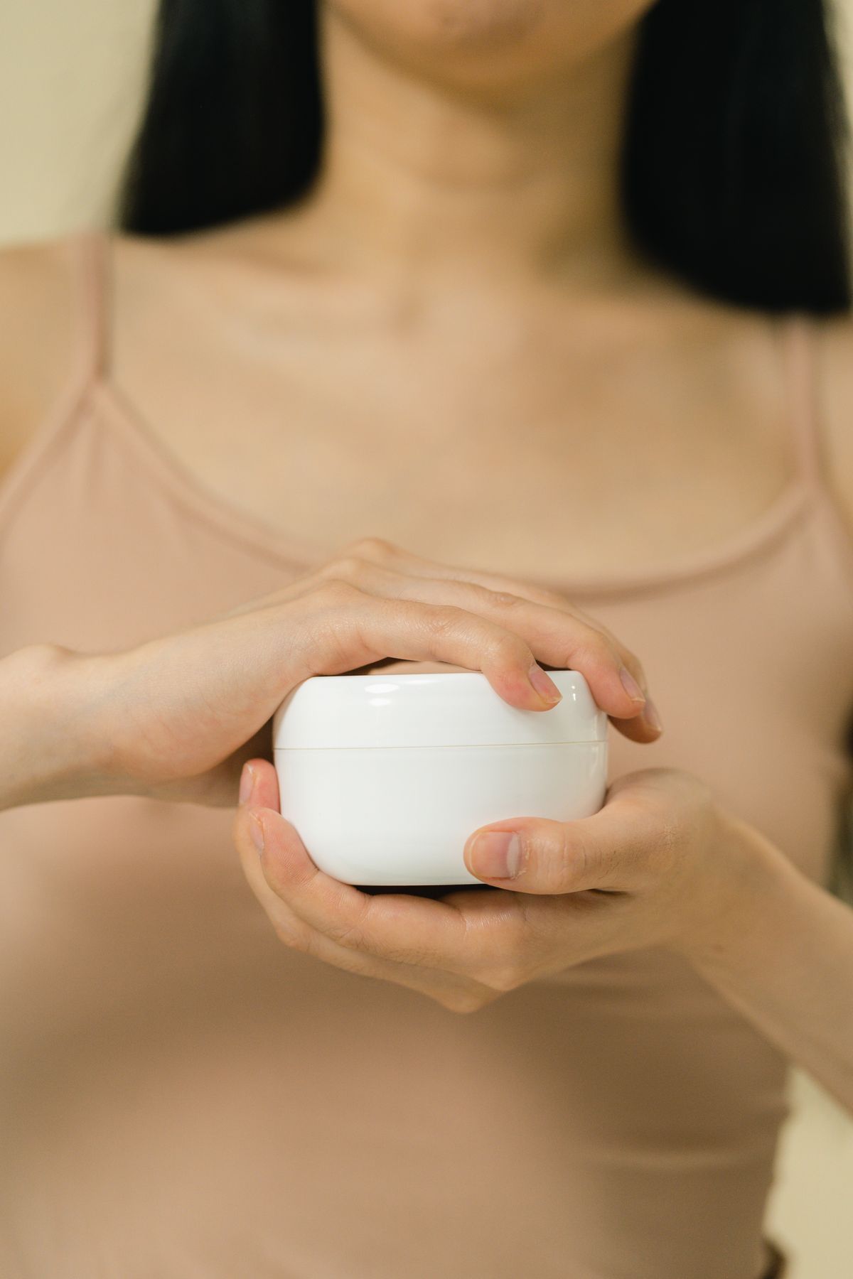 Hands holding a small white jar of skincare cream